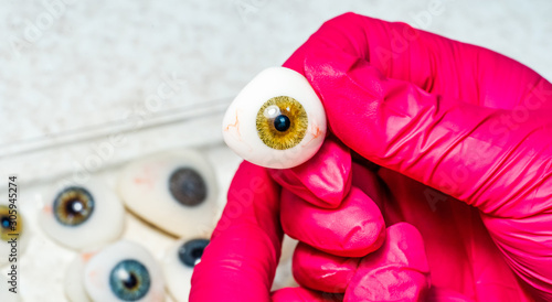 Ophthalmologist or surgeon holds an eye, eyeball prosthesis in hands . Concept photo for ocular prosthesis, diagnosis treatment of ophthalmic diseases, surgical operations on eyes. Closeup.