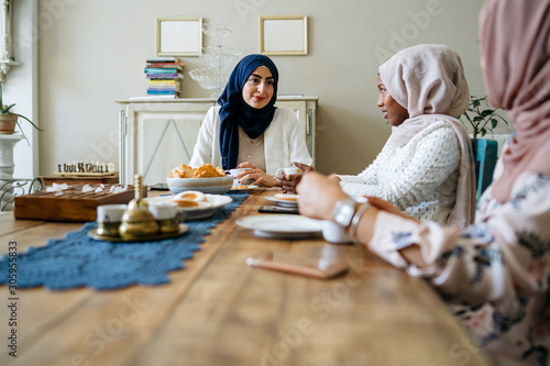 Three young muslim women drinking tea at the kitchen table - Arabian Millennials at a time of relaxation at home