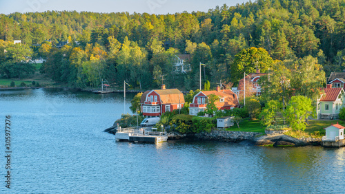 Rocky coast of Stockholm archipelago in Baltic sea with traditional white and red houses at sunny autumn evening with a fall scenery.