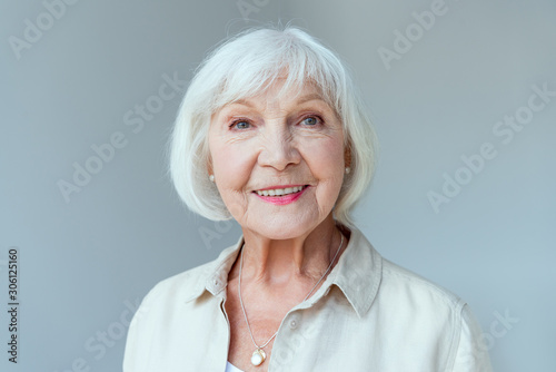 attractive and smiling woman looking at camera isolated on grey