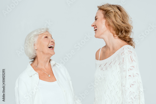 attractive mother and daughter smiling and looking at each other isolated on grey