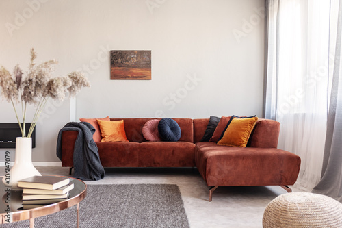 Real photo of warm color cushions on a red couch standing next to the window in cozy living room interior