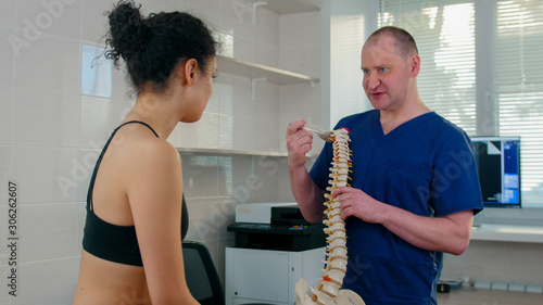 Chiropractic treatment - the doctor inspecting the young woman before the session - showing the problems on the spine sample