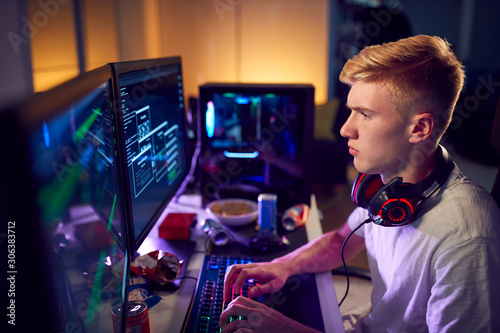 Male Teenage Hacker Sitting In Front Of Computer Screens Bypassing Cyber Security