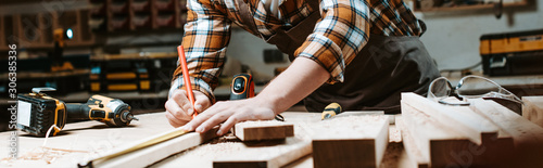 Panoramic shot of woodworker measuring wooden plank