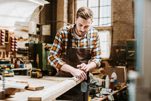 Selective focus of bearded woodworker holding chisel while carving wood in workshop