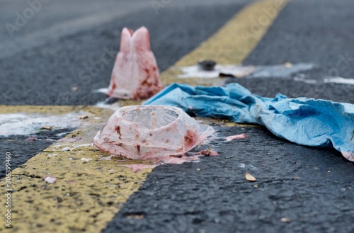 Trash scattered on the asphalt in a parking lot on intersecting yellow lines. Image taken close up at ground level with room for text.