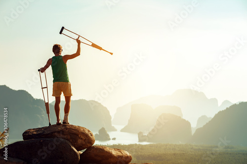 Disabled man with crutches stands on big rock