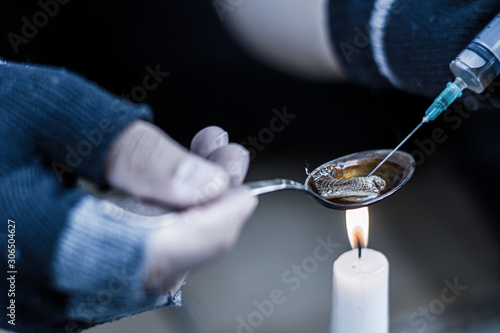 Closeup male hands in black fingerless gloves are preparing dose of heroin for injection. Addict junkie man is going to take narcotic substance in abandoned building. Drug addiction concept.