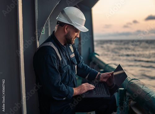 Marine chief officer or captain on deck of vessel or ship watching laptop. Internet and home connection at sea.