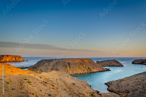 Serene landscape of mountains and sea with the golden rays of the sunrise over the horizon. From Muscat, Oman.
