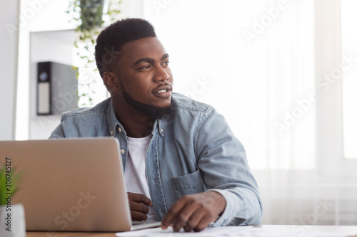 Portrait of pensive afro businessman sitting at workplace in modern office