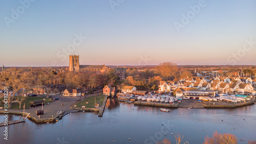 An aerial view of a river at golden hour with grassy bank and majestic church and marina in the background under a majestic blue sky