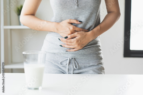 lactose intolerance concept. Woman holding a glass of milk and having a stomachache.