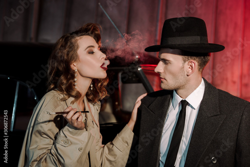 attractive woman smoking cigarette near handsome gangster in hat