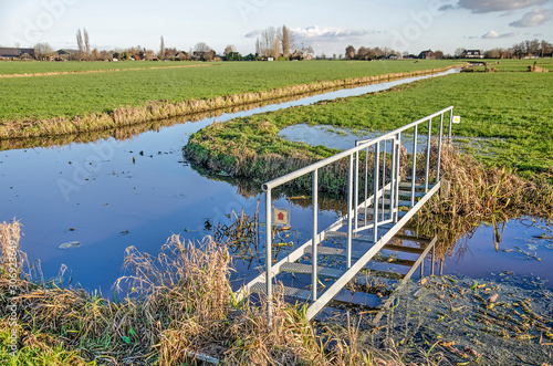 Minimalistic steel bridge as part of a muddy hiking trail through the polders of the Green Heart of the Netherlands near the town of Bodegraven