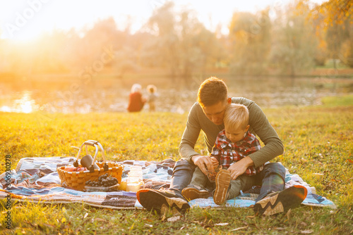 A dad and his son are having picnic together near a lake in park.