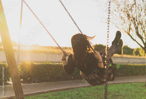 Girl having fun on the swing - young millenial woman relaxes in the park - concept of freedom and well-being - warm color with sunny golden light