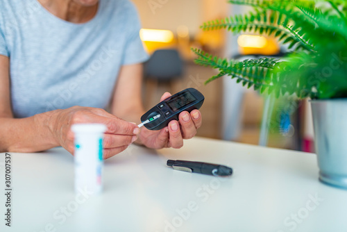 Checking the glucose level with a glucometer. Woman using digital glucometer on light background. Diabetes monitoring. Diabetes doing blood glucose measurement. Woman using lancet and glucometer.