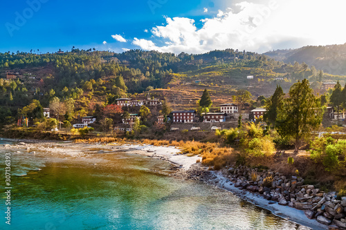 Mo Chhu River on a nice sunny day, Punakha, Bhutan. View from the wooden cantilever bridge near Punakha Dzong to river, houses of Punakha city and Himalaya mountains covered with forest.