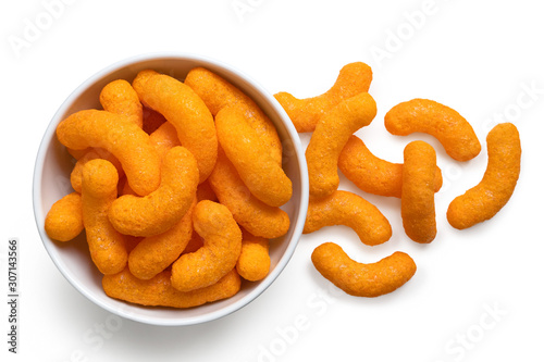 Extruded cheese puffs in a white ceramic bowl next to spilled cheese puffs isolated on white. Top view.