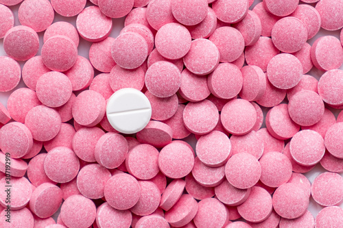 Pile of pink pills and around a white one. Medication, self-treatment or placebo concept: one tablet is different from the lot of others