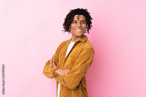 Young African American man with corduroy jacket over isolated pink background with arms crossed and happy