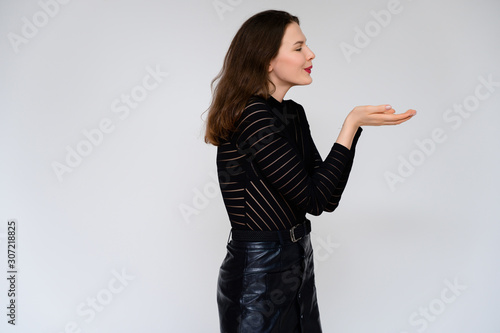 Concept adult girl on a white background. A photo of a pretty brunette girl in a black skirt and black sweater smiles and shows different emotions in different poses right in front of the camera.