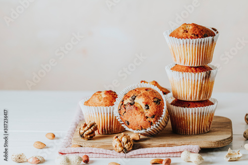 Vanilla caramel muffins in paper cups on white wooden background. Delicious cupcake with raisins, almonds and nuts. Homemade biscuit cakes. Copy space for text.