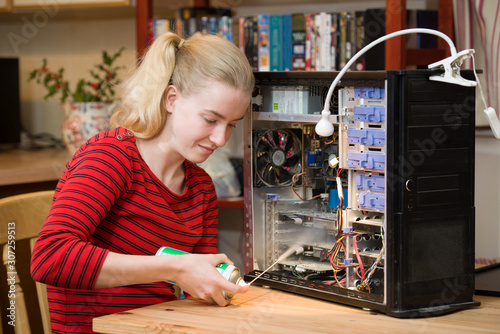 Teenage girl using a can of compressed air to clean the inside of a PC