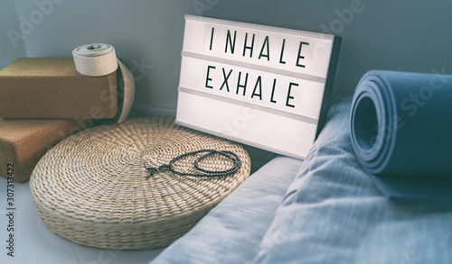 Yoga breathing INHALE EXHALE sign at fitness class on lightbox inspirational message with exercise mat, mala beads, meditation pillow. Accessories for fit home lifestyle.