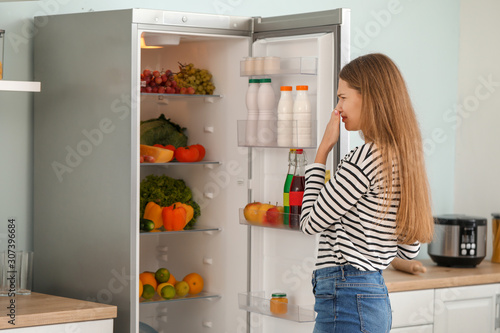 Woman feeling bad smell from fridge in kitchen