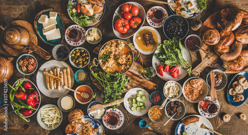 Turkish breakfast table. Flat-lay of fresh pastries, vegetables, greens, olives, cheeses, fried eggs, jams, honey, tea in copper pot and tulip glasses, top view. Middle Eastern meal