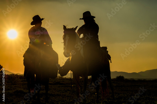 Two cowboys riding horseback at sunset with yellow sky