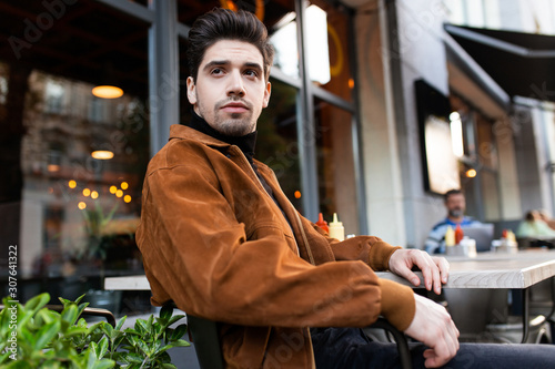 Young handsome man thoughtfully looking away resting in cafe on street
