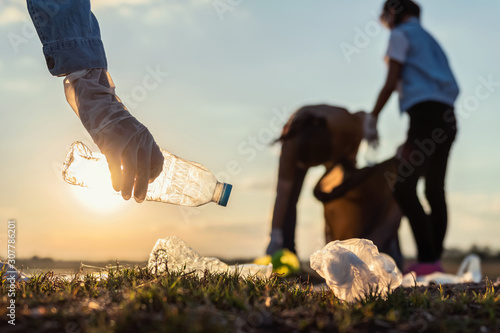 people volunteer keeping garbage plastic bottle into black bag at park river in sunset