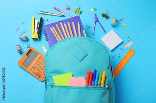 Stylish backpack with different school stationery on light blue background, flat lay