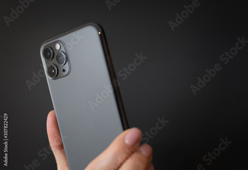 Person holding modern smartphone with tripe lens camera in hand on dark background