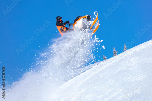 snowmobile jump straight up. the guy is flying and jumping on a snowmobile on a background of blue sky leaving a trail of splashes of white snow. bright snowmobile and suit. No brands. copy text