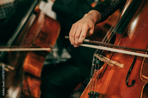 Symphony orchestra on stage, hands playing cello. Shallow depth of field, vintage style.