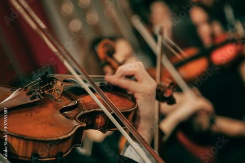 Symphony orchestra on stage, hands playing violin. Shallow depth of field, vintage style.