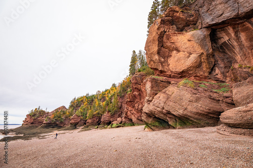 A tourist taking a picture is dwarfed by the massive sandstone rock formations during low tide at Hopewell Rocks, New Bruswick, Canada