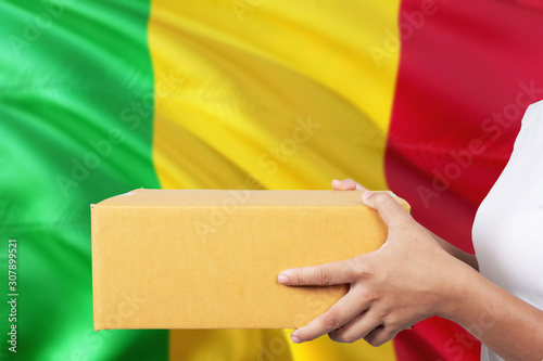 Mali delivery service. International shipment theme. Woman courier hand holding brown box isolated on national flag background.