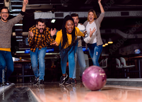 Group of friends enjoying time together laughing and cheering while bowling at club.