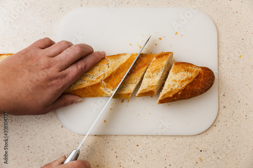 pan baguette de harina cortado a cuchillo encima de tabla de corte, en mármol claro.