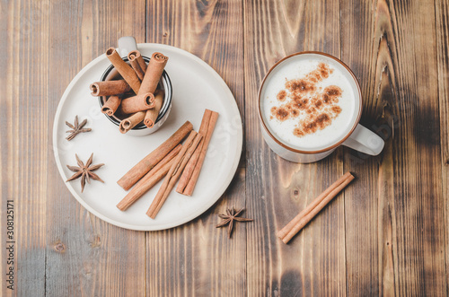 Eggnog. Traditional christmas cocktail in a mug and cinnamon sticks and anise on a white bowl on a wooden background. Top view.