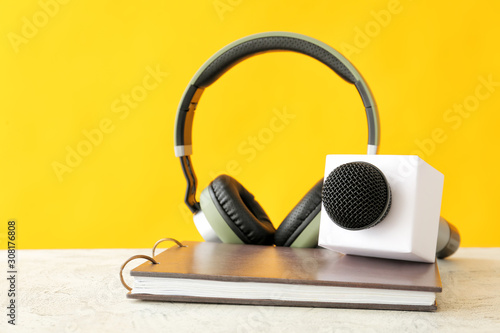 Microphone, headphones and notebook on table against color background