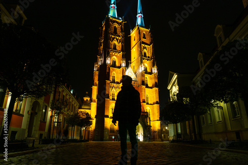 Wroclaw. Silhouette of a traveller man with backpack in front of illuminated cathedral of St. John the Baptist on Ostrow Tumski