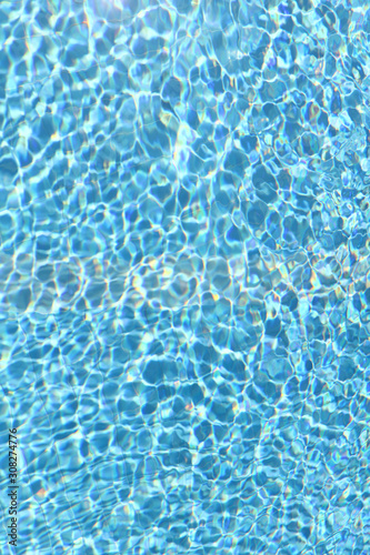 Background of pool water texture. Reflection of sun rays in pool water. Vertical, close-up, cropped shot. Sports and recreation concept.