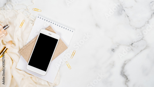 Feminine workspace concept. Top view white marble background with fashion accessories, office supplies and smartphone. Minimal flat lay style composition. Beauty blogger desk table concept